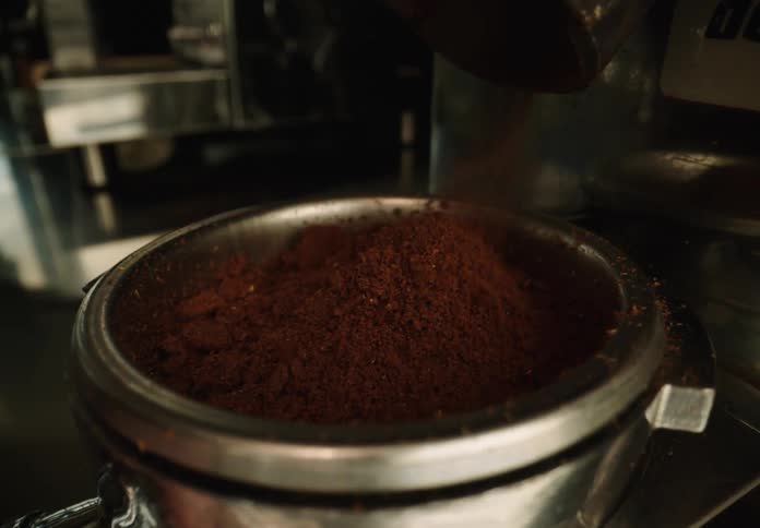 Pouring coffee grounds inside an espresso machine portafilter