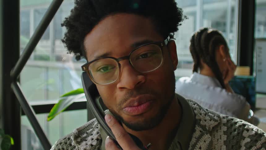 Portrait of a man finishing a phone call and right behind is a woman working in an office with her back turned