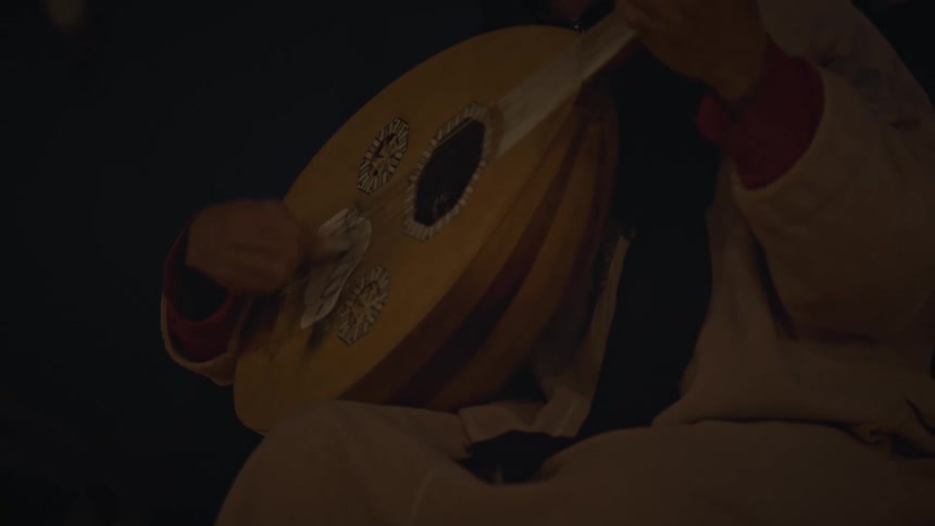 A person is sitting outdoors in the night while playing a musical instrument
