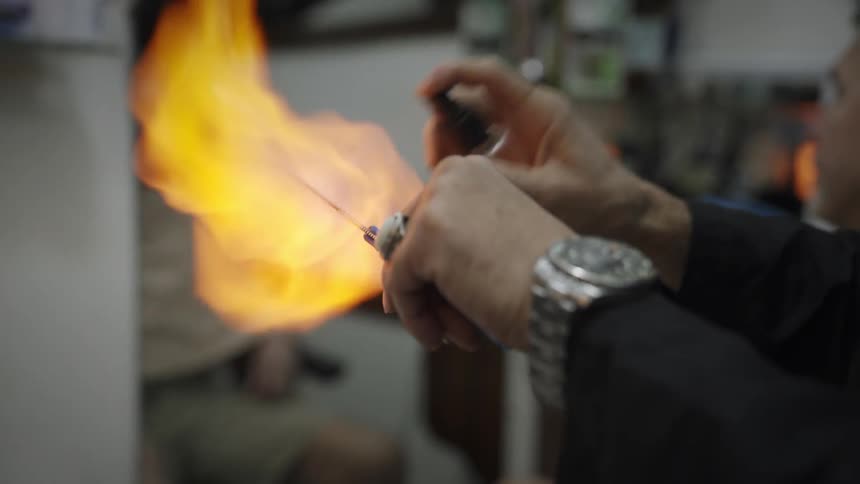 A barber disinfecting a blade using alcohol and a flame