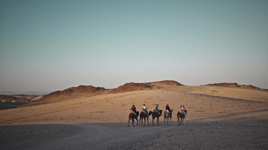 Group of people riding camels through the desert one morning