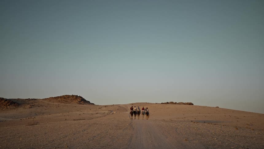 A group of people are riding horses through the desert