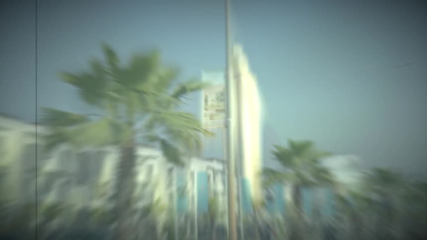 View of a street with palm trees and next to a hotel with a large tower