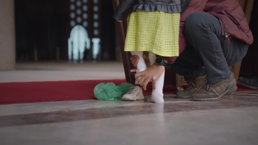 An adult helps a little girl to take off her shoes to enter a mosque