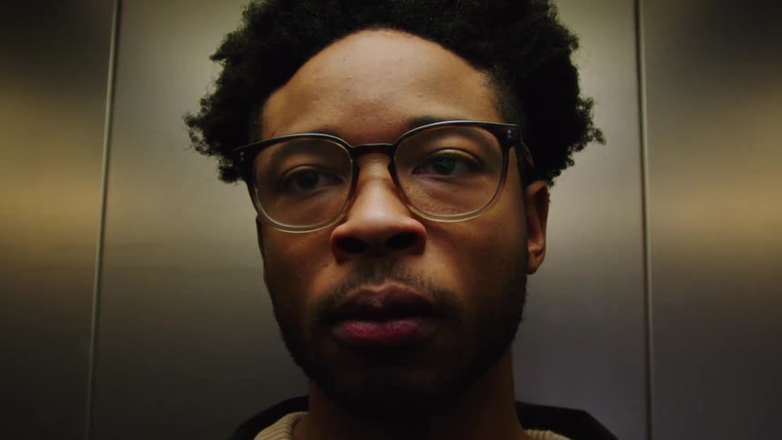 A man is wearing glasses and standing inside an elevator