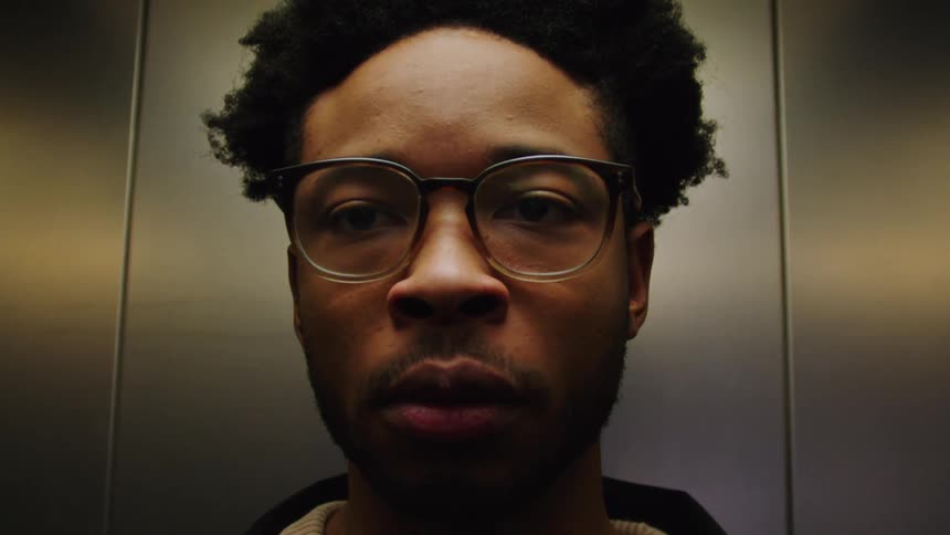 Portrait of a man inside an elevator adjusting his prescription glasses and leaving