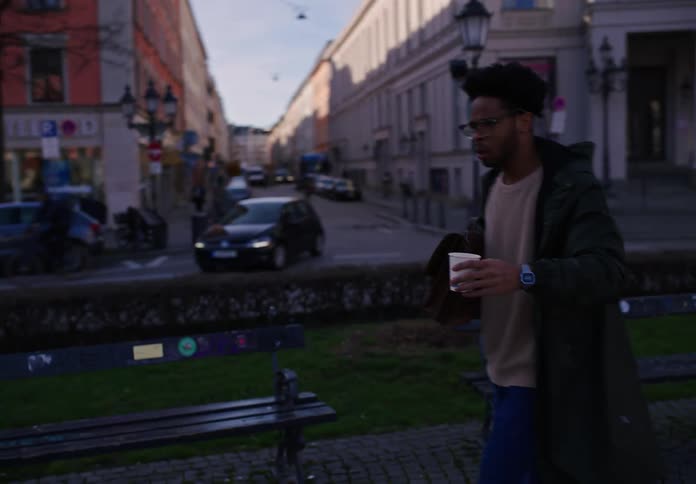 Man clutches a briefcase and paper cup while running past benches in the town square