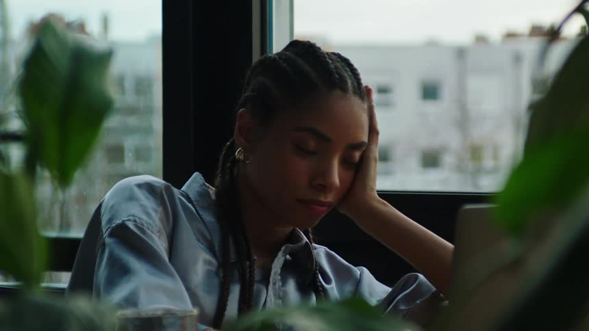 Woman sitting down indoors resting her hand on her face