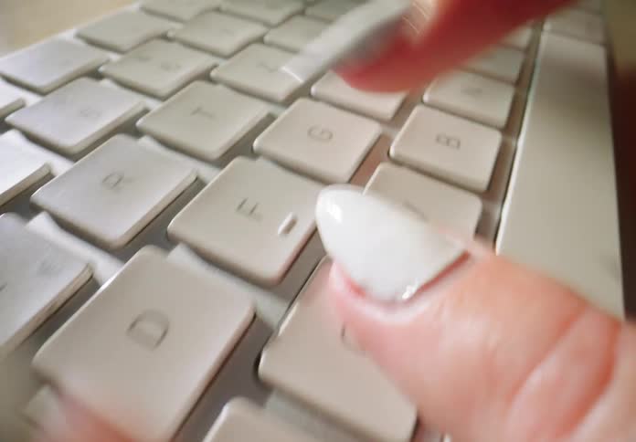 Female wearing white nail polish and typing on a computer