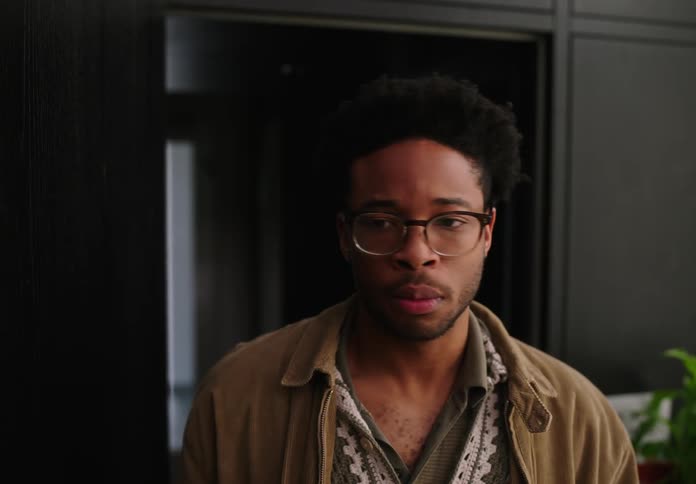 Man entering from behind a solid wood door looks around with a look of slight confusion adjusts glasses turns and walks off