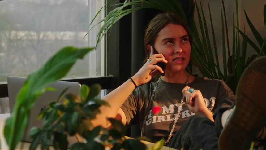 Woman is talking on the phone and sitting next to decorative plants