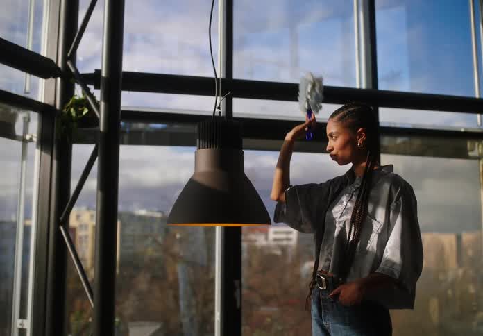 A woman dusts a lamp in the office while his coworker brings coffee