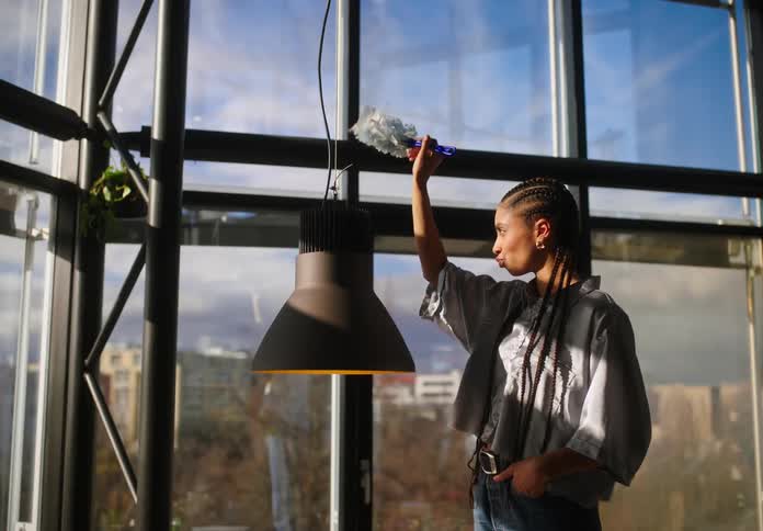 A woman dusts a hanging light before a man offers her a cup of coffee