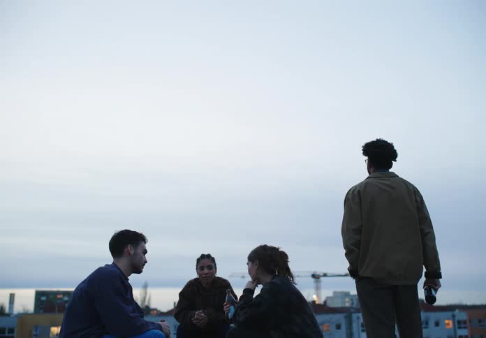 A group of friends drink beer on the roof of a building in the city