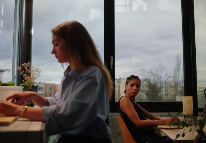 Woman at a counter cutting potatoes and next to her another woman looks at her with an impressed facial expression while they are in a work environment
