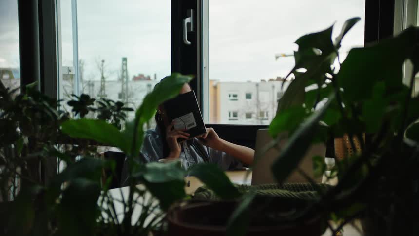 Woman sitting at office desk bored putting notebook in her face
