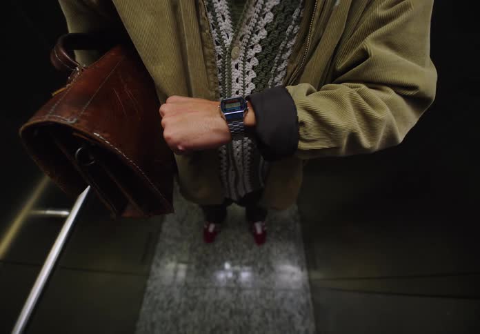 Man on an elevator checks his breath and the time on his wristwatch