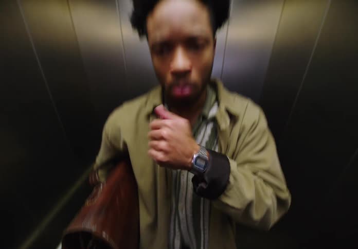 A man riding an elevator checks his breath and the time on his wristwatch