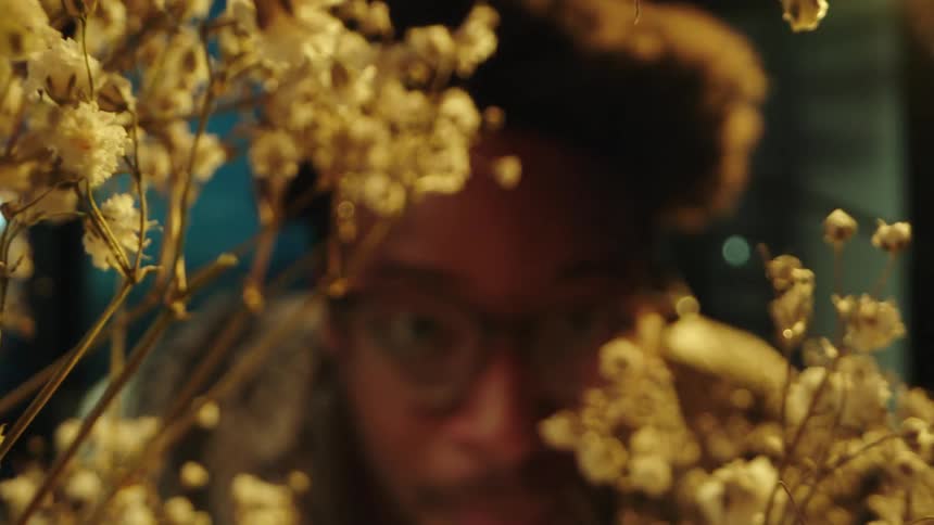 White flower illuminated by yellow light and a man watering with a spray bottle