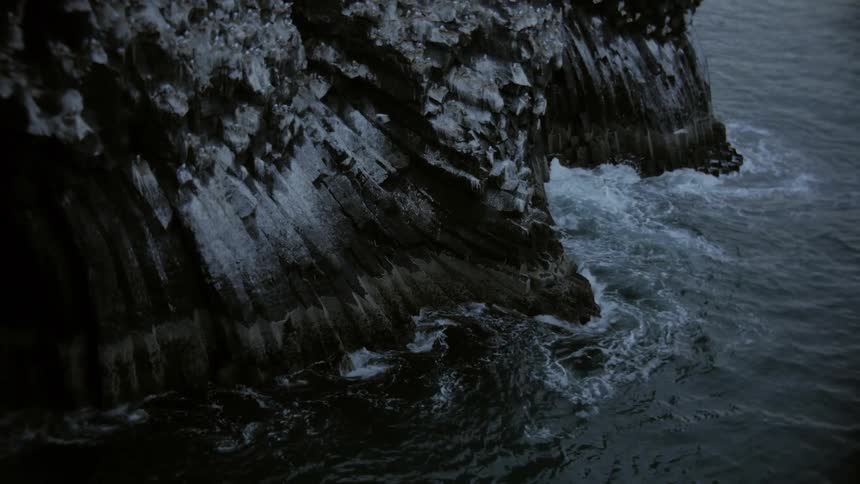 Birds are flying above the ocean near the sides of a cliff