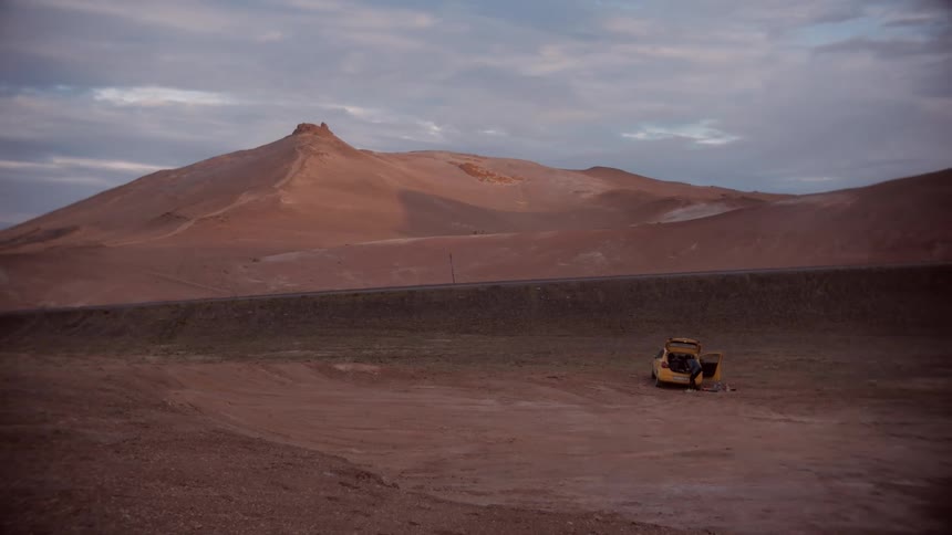 A person next to a yellow car in the middle of the desert