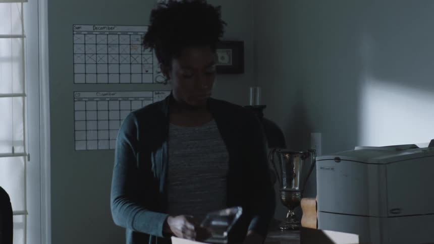 Woman in a room taking a small trophy and putting it inside a box with a sad facial expression