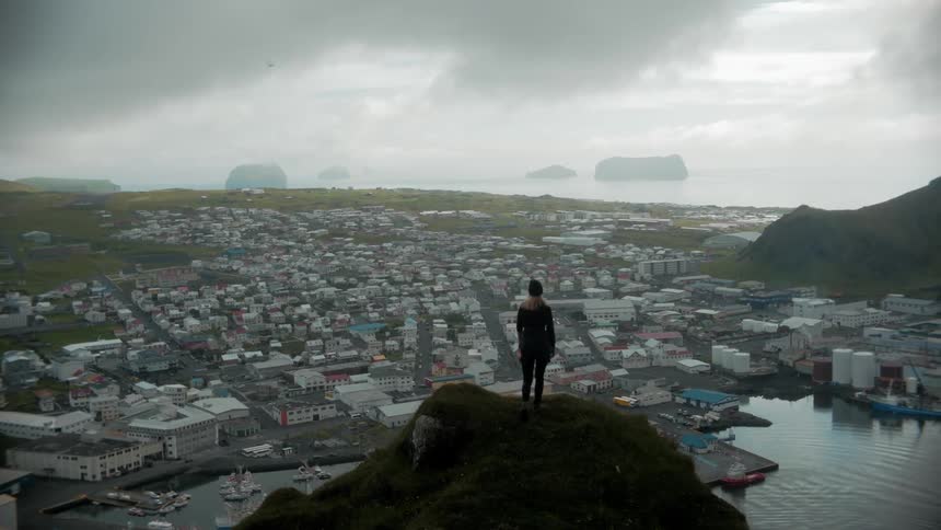 Panorama of a woman on the peak of a cliff placing her hands on her head enjoying a view of the sea and a city