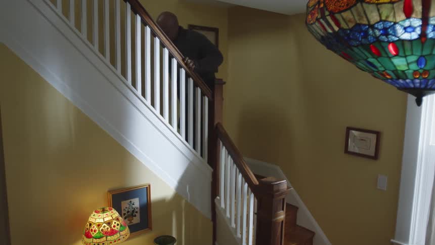 An old black man climbs stairs in a house