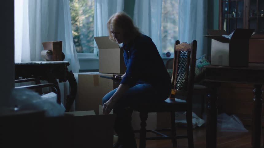 Woman taking a picture frame in the room wrapping it in bubble wrap and putting it in a box with sad facial expression