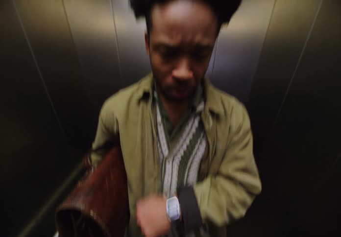 A man in an elevator looks at his watch and leaves