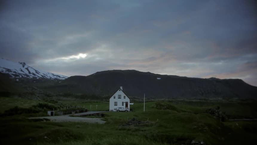House in a rural field with mountains in the background on a cloudy morning