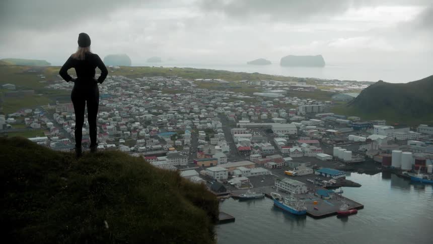 A white woman looks down at a small coastal city