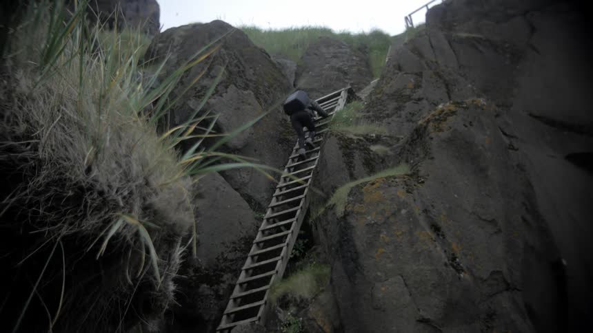 A person is climbing down a ladder near a cliff