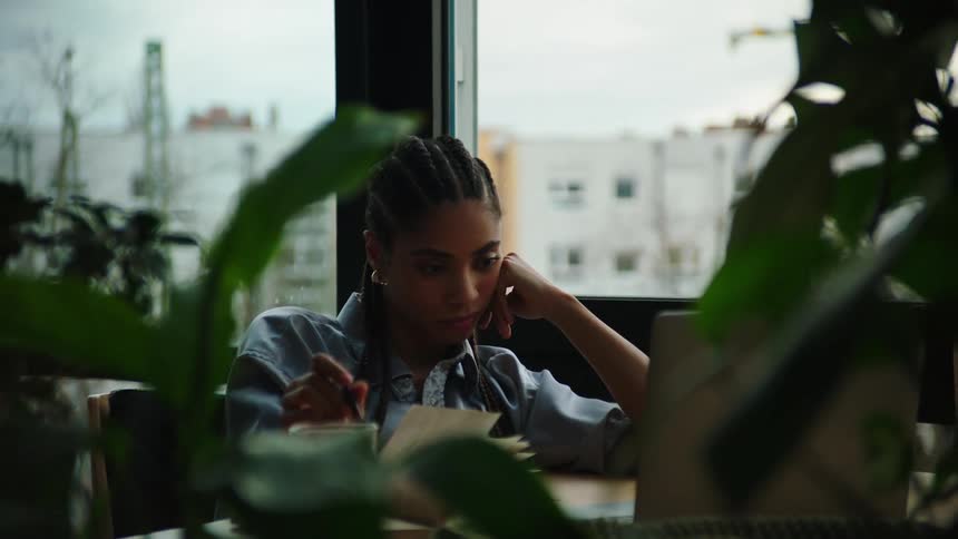 A young woman deep in thought while studying she twirls her pen tapping it on the table