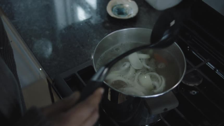 Man with the help of a spatula preparing soup in a pan on the stove