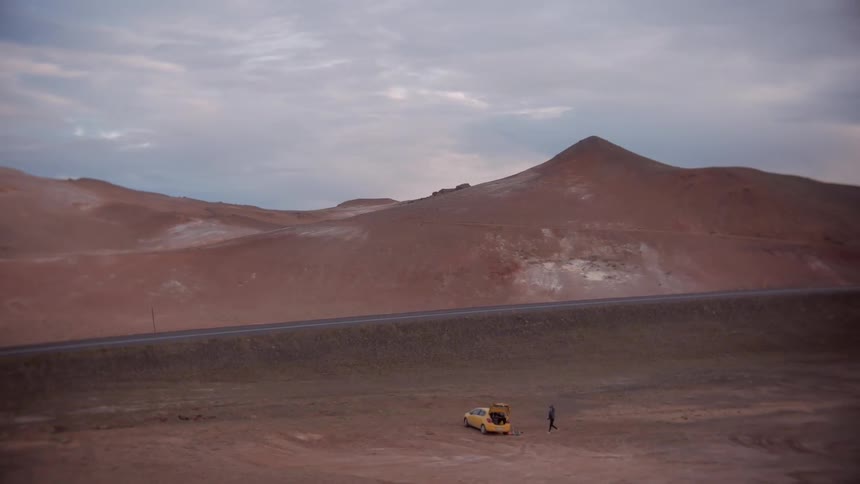 A person stands around a yellow car in the desert