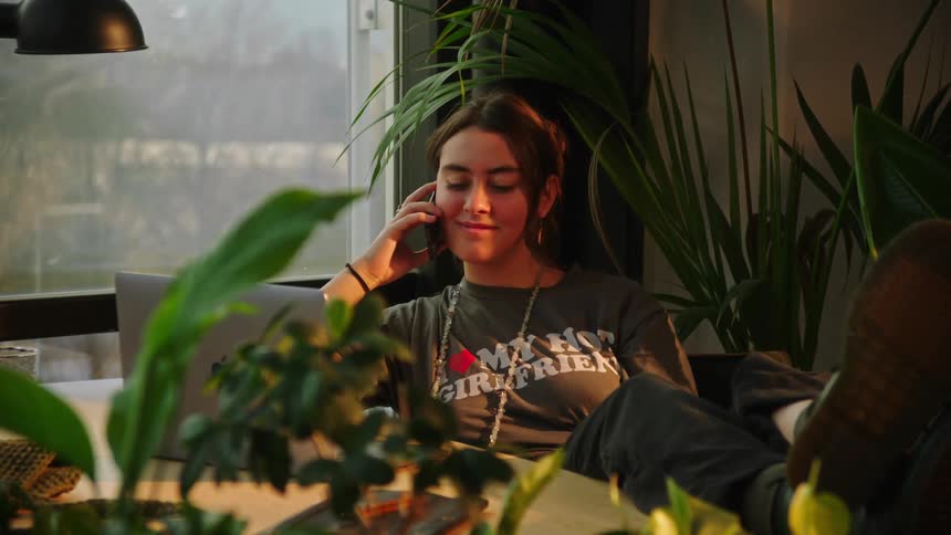 Woman sitting at a desk next to plants and talking on a cellphone