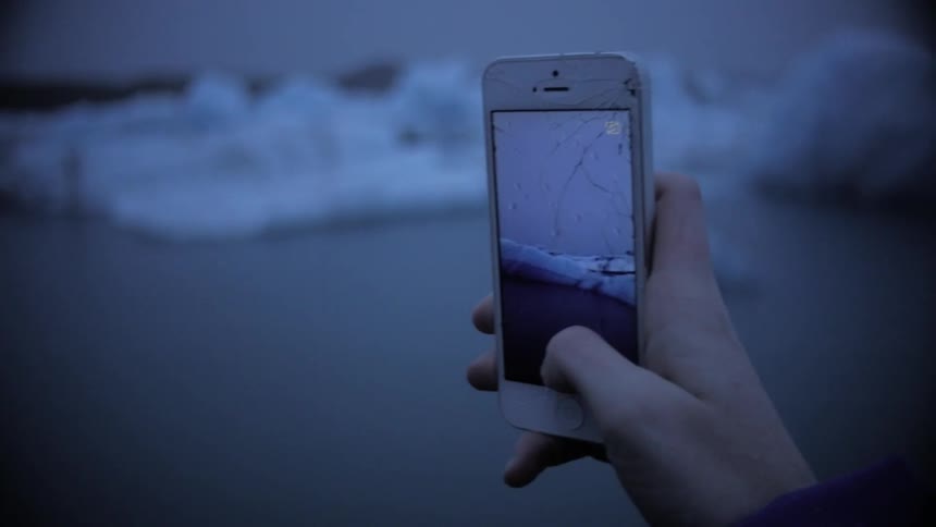 Person recording an iceberg from a cellphone with a cracked screen