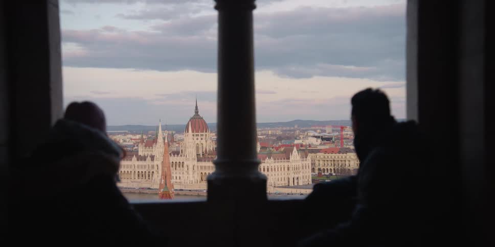 Silhouette of a man and a woman enjoying the view of Budapest over the Danube through the window