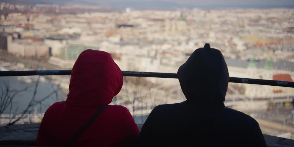 Two people sit near rail overlooking Elizabeth bridge crossing the Danube River on Budapest waterfront