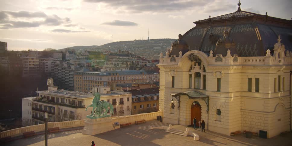 People walking into Buda Castle Riding Hall in Budapest with city view in the background