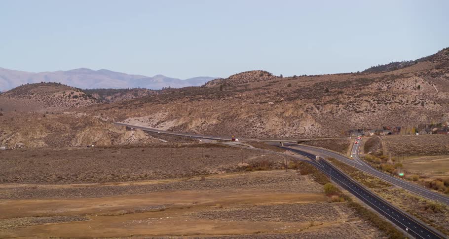 Vehicles drive along highways passing town in arid terrain near mountains