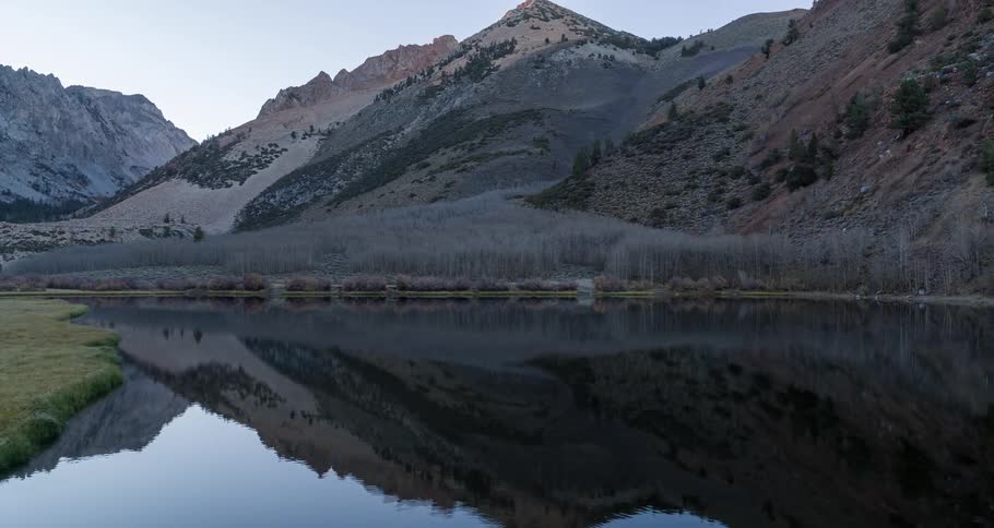 A small lake reflecting a mountain and there is a field with lots of vegetation next to it