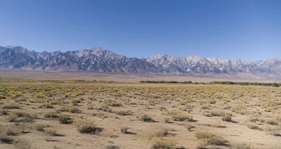 Arid rural countryside borders snowy mountain range on a sunny day