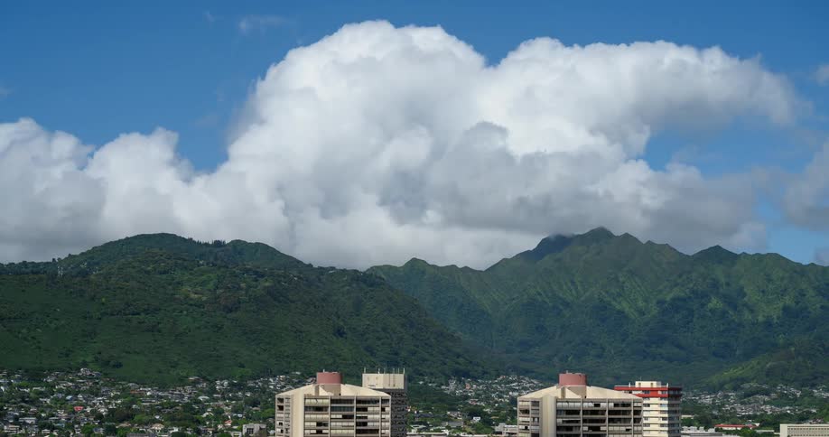 White clouds passing over city near mountains cast shadows across buildings