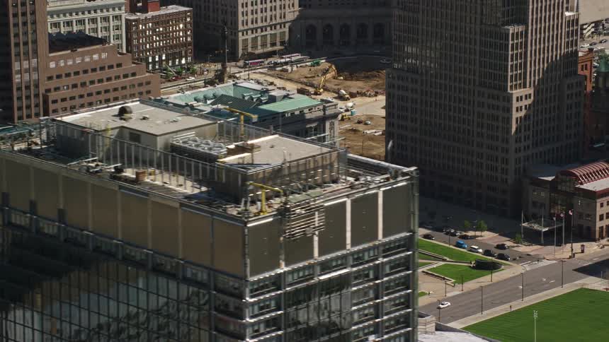 Cars drive by a park surrounded by downtown city buildings