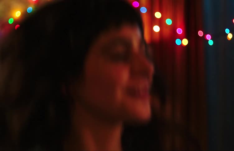 Teenager smiles while dancing in room decorated with a strand of colored lights