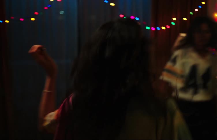 Two young women dancing in the living room and the friend throwing popcorn into the others mouth while having fun
