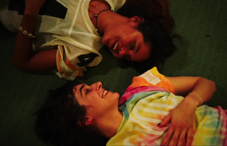 Two young women laugh while talking laying on the floor