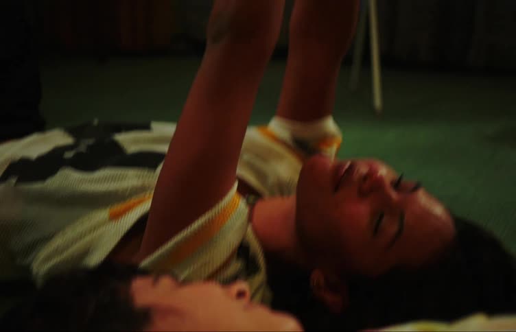 Two young women lying on the floor head to head with each other smiling moving their heads and their hands to music